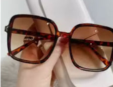 Tortoiseshell sunglasses held by a hand against a white background