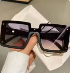 Black sunglasses held by a hand with a white sleeve on a light gray background
