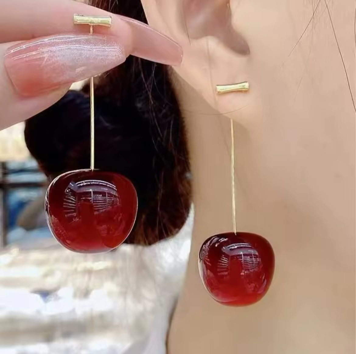 Red cherry-shaped earrings being worn with a blurred background