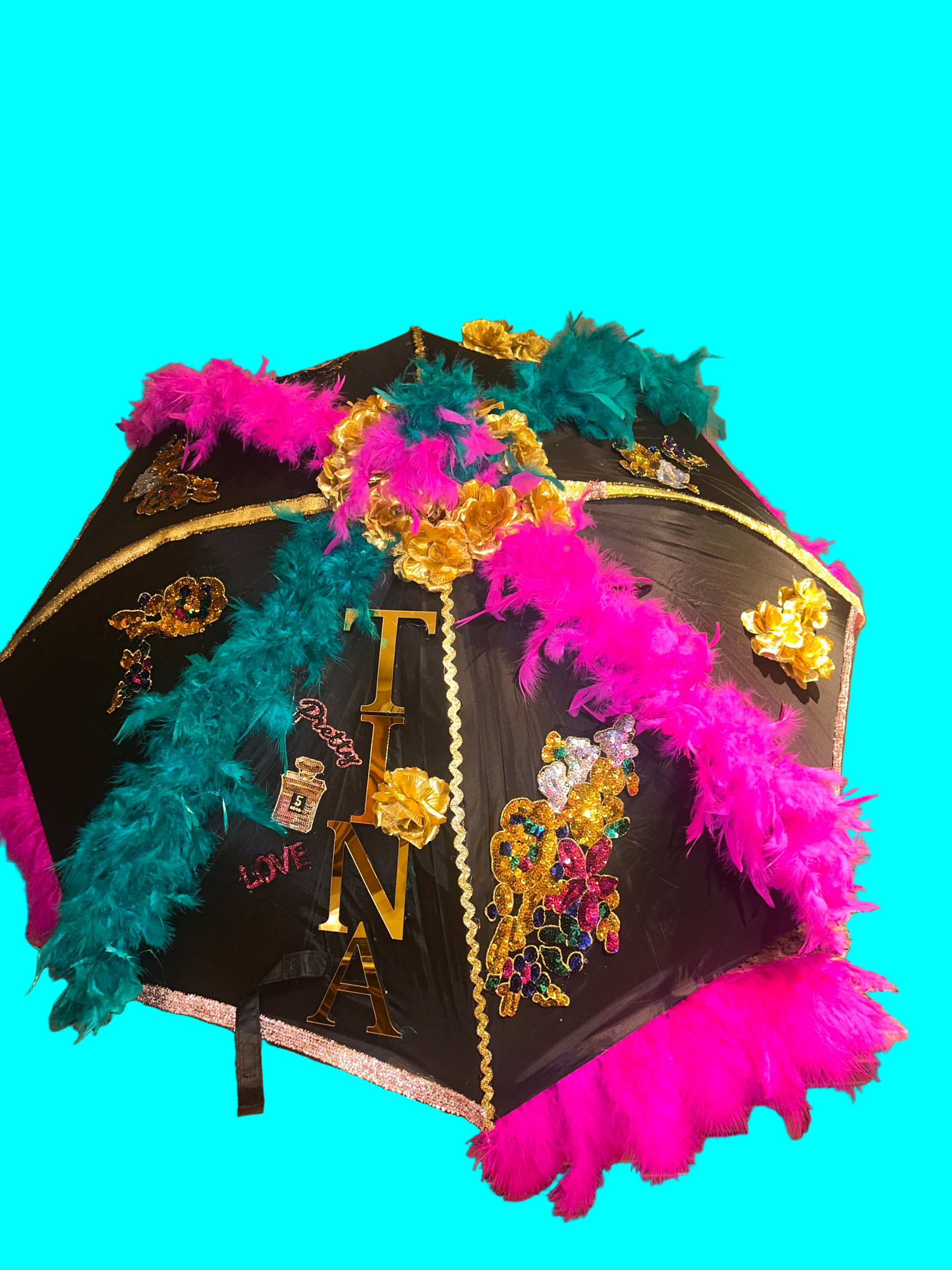 Decorative umbrella with colorful feathers and gold accents against a neutral wall.